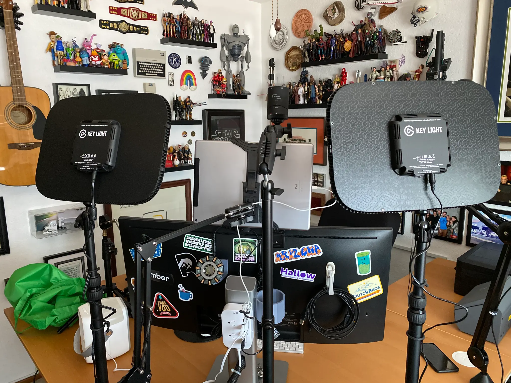 Rob Kubasko's podcast studio: two Elgato Key Lights flanking sticker-covered monitors, action figures lining every shelf, guitar on the wall.