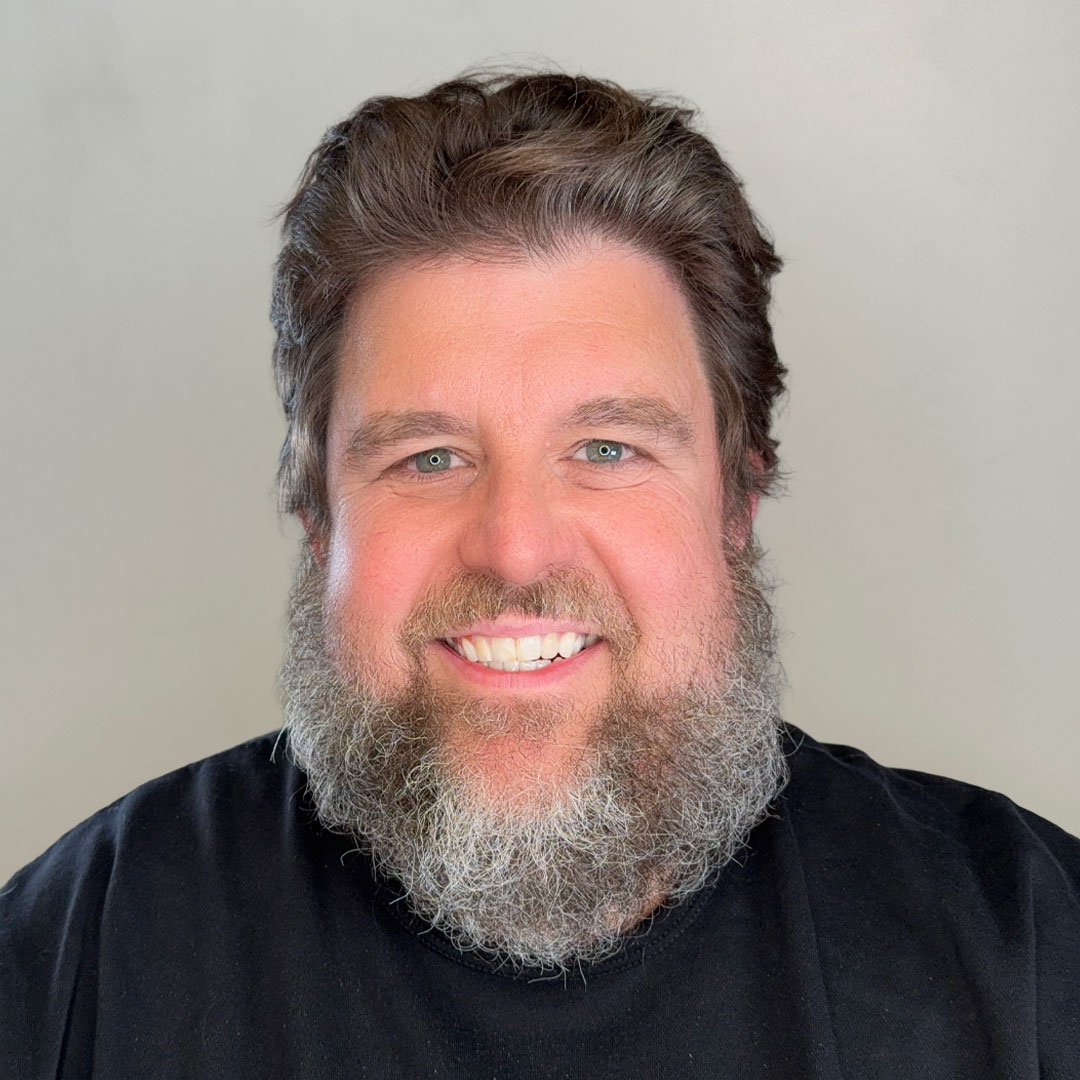 A present-day photograph of Rob Kubasko, smiling, in a dark t-shirt, with a short beard, in a parish setting.